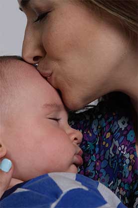 A mother gently kissing her sleeping baby's forehead.